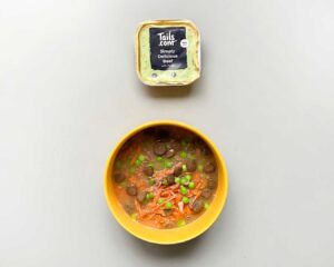 Top down image of yellow dog bowl with beef broth recipe inside, wet food tray above bowl