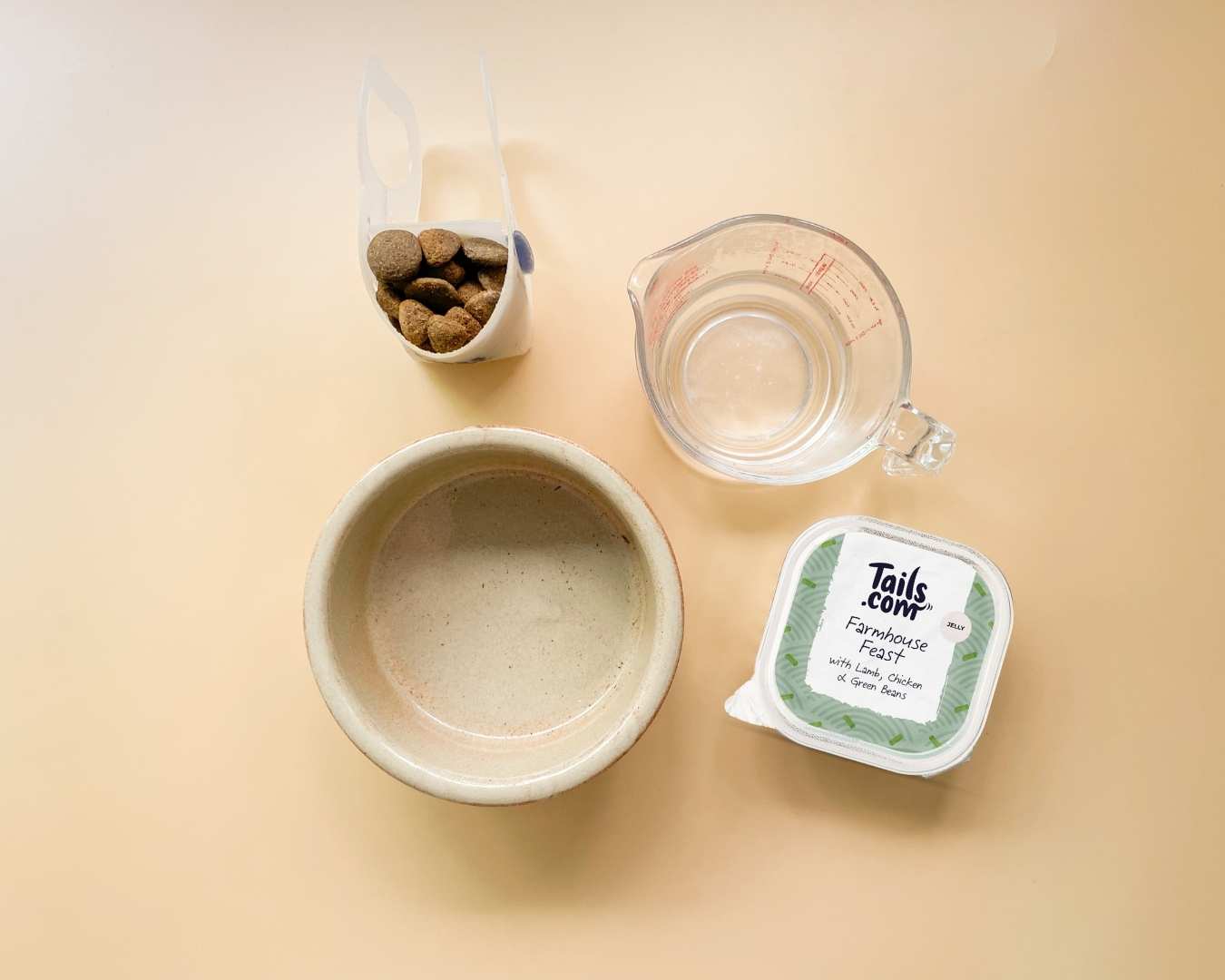 Top down picture of ingredients: dog bowl, scoop filled with kibble, jug with water and wet food tray