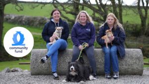Three women from Refuge4Pets charity sitting on a bench with 3 dogs, tails.com Community Fund logo of crossing dog tails on lefthand side