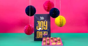 tails.com Christmas Countdown Advent Calendar for dogs standing upright, with star and paw-shaped biscuits lined up in front and pink, blue and yellow pompoms hanging from the ceiling
