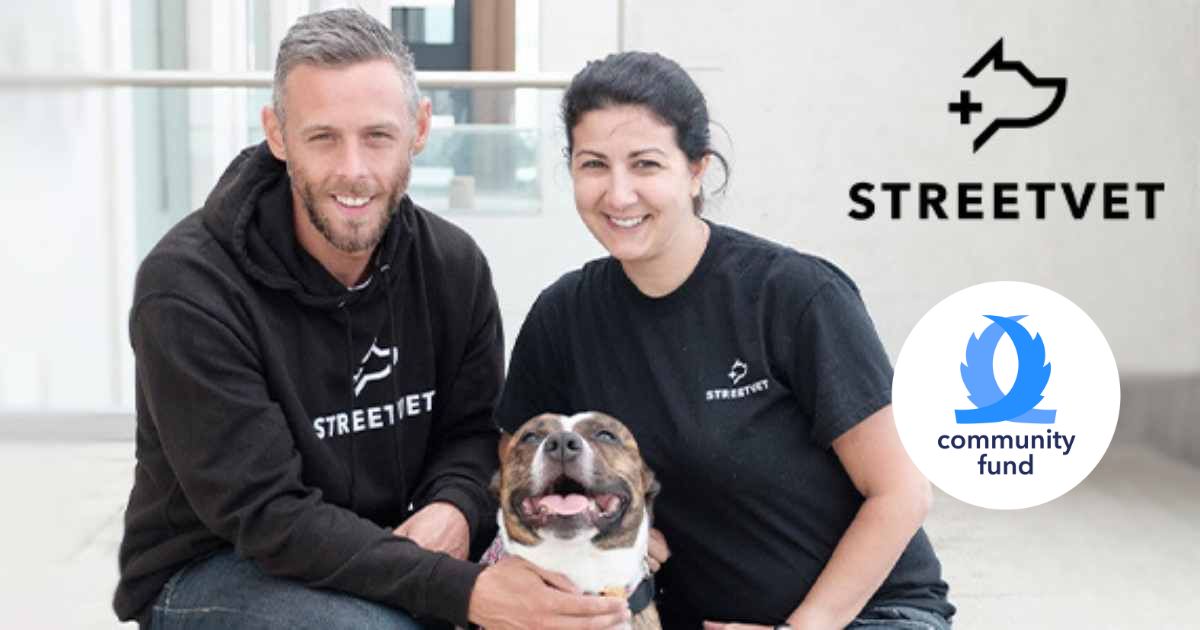 StreetVet charity co-founders Jade and Sam wearing black StreetVet hoodies, kneeling down while stroking Bailey the brown and white Staffordshire terrier and StreetVet graduate. StreetVet and tails.com Community Fund logos on right side