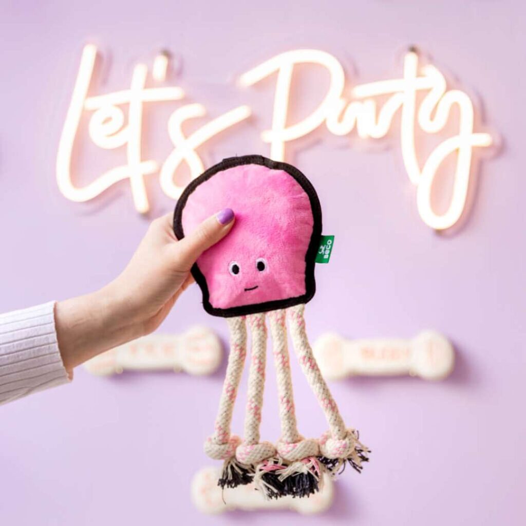 Ollie the Octopus squeaky toy being held up in front of a pink wall with a light up sign saying "Let's Party"
